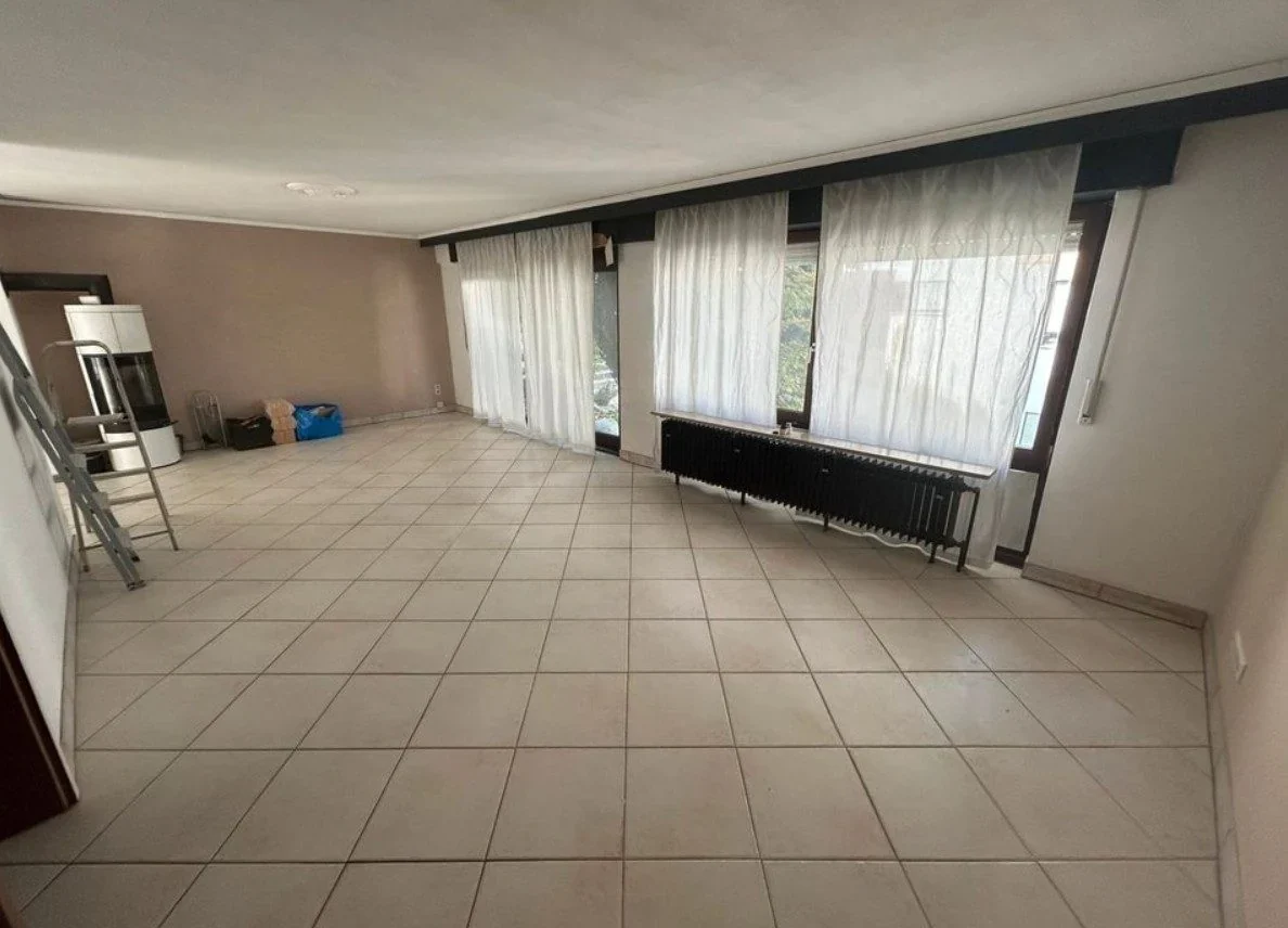 Vorher: dunkles Handyfoto eines leeren Wohnzimmers, Fensterwand angeschnitten